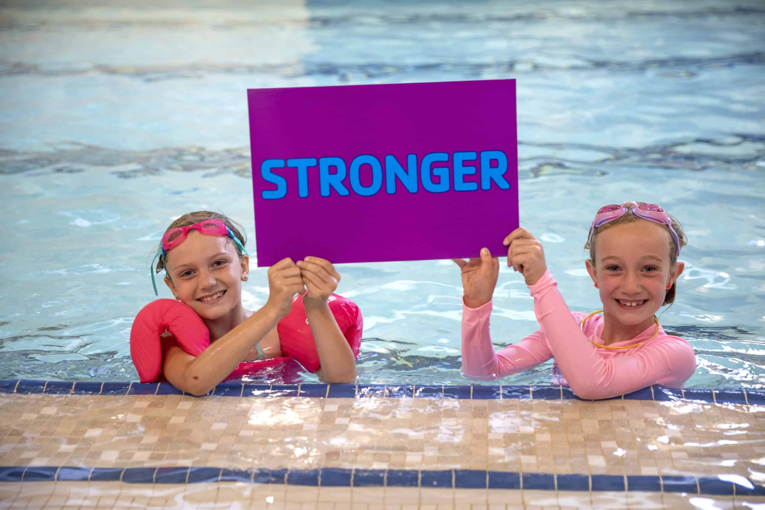 two girls in a pool holding a sign