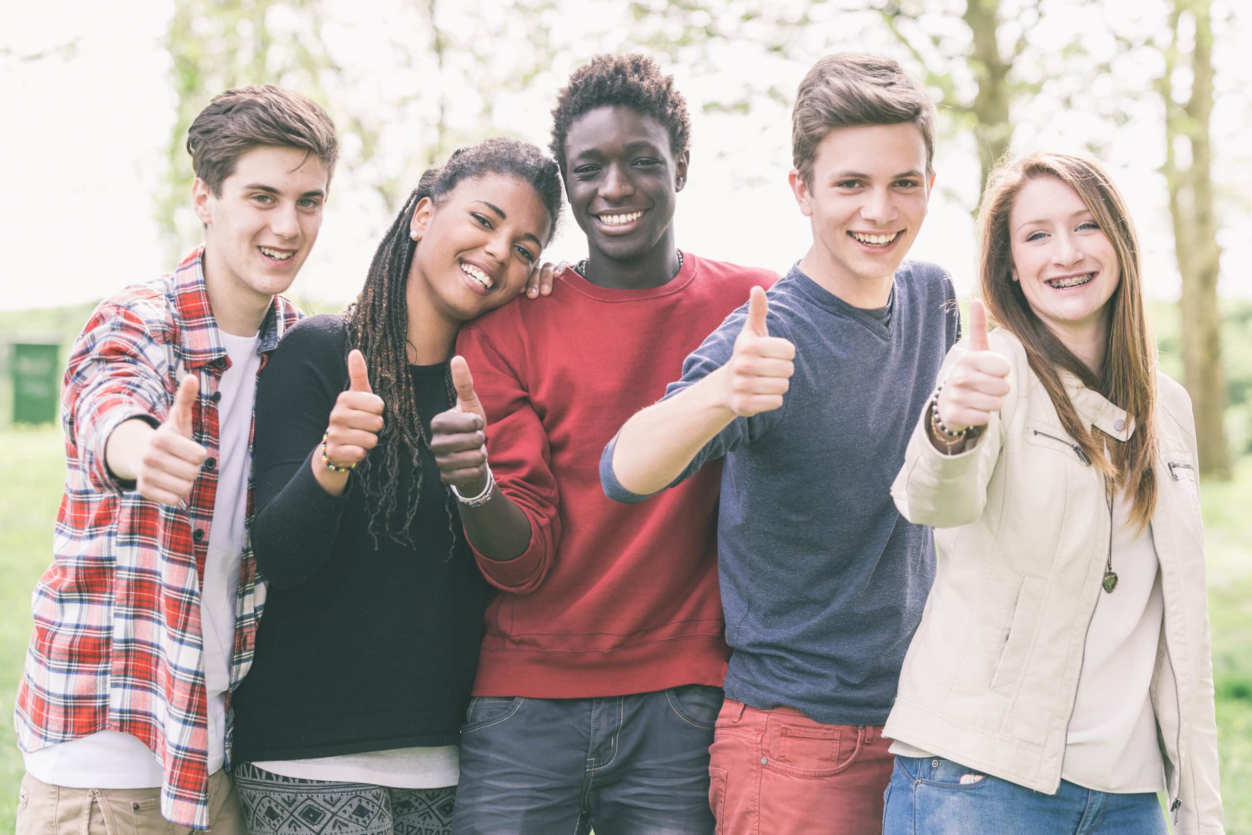 A group of five diverse teenagers, including two girls and three boys, are standing together and smiling. They are all giving thumbs up signs. | Membership Rates